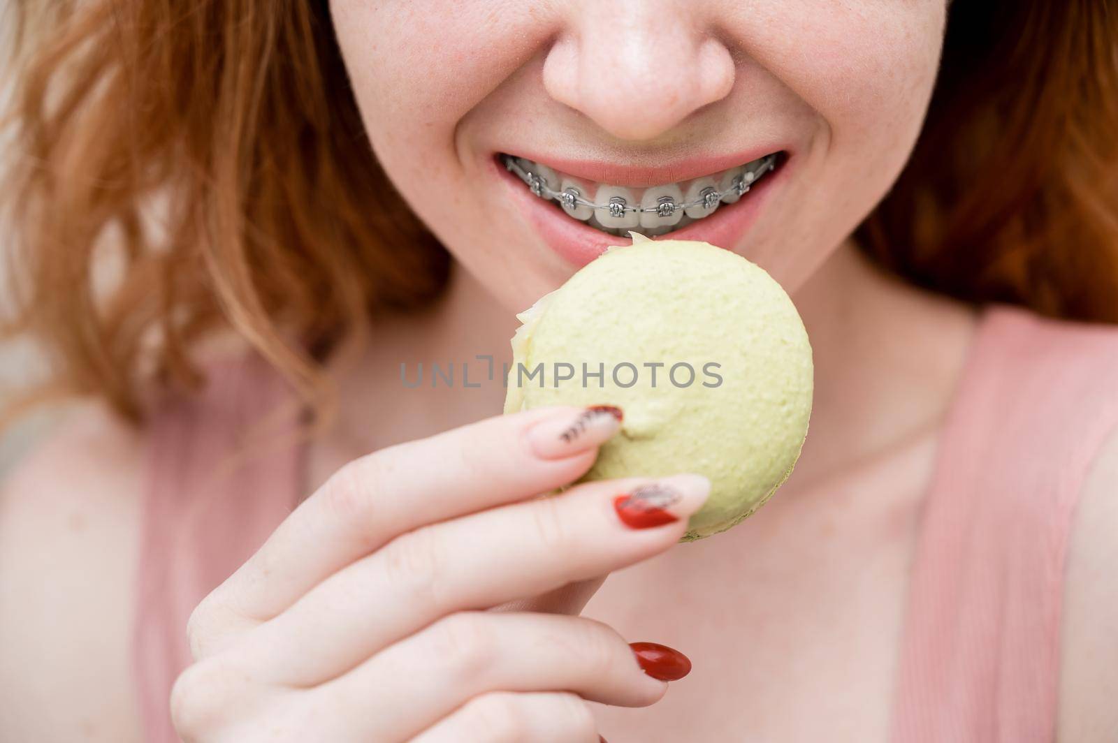 Young red-haired woman with braces eating macaron cake