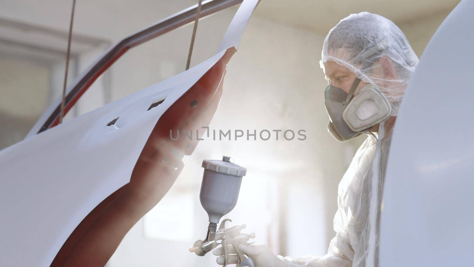 Car manufacturing factory. Painting Spray Paint vehicle parts at car service workshop. Industrial spray painting process. Man painting a car in a body shop.