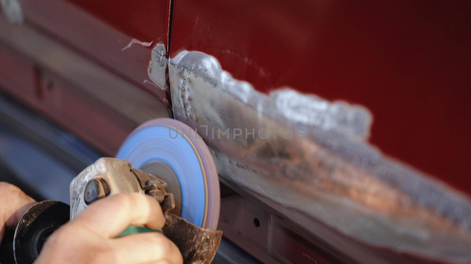 Close-up of worker grinds car damage. Hard grinding is designed to smooth out irregularities. Professional auto workshop worker grinds dented door of car.
