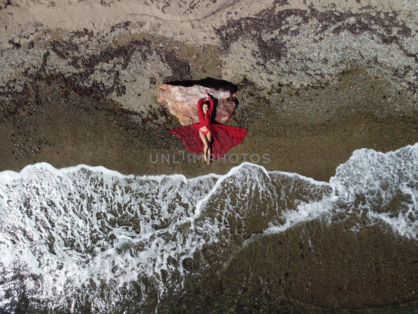 Young sensual blonde woman sitting on the rock near water at sea and enjoys the sea waves on background of two volcanic rocks, like in Iceland. Dreams holidays and weekend vacation in summer time