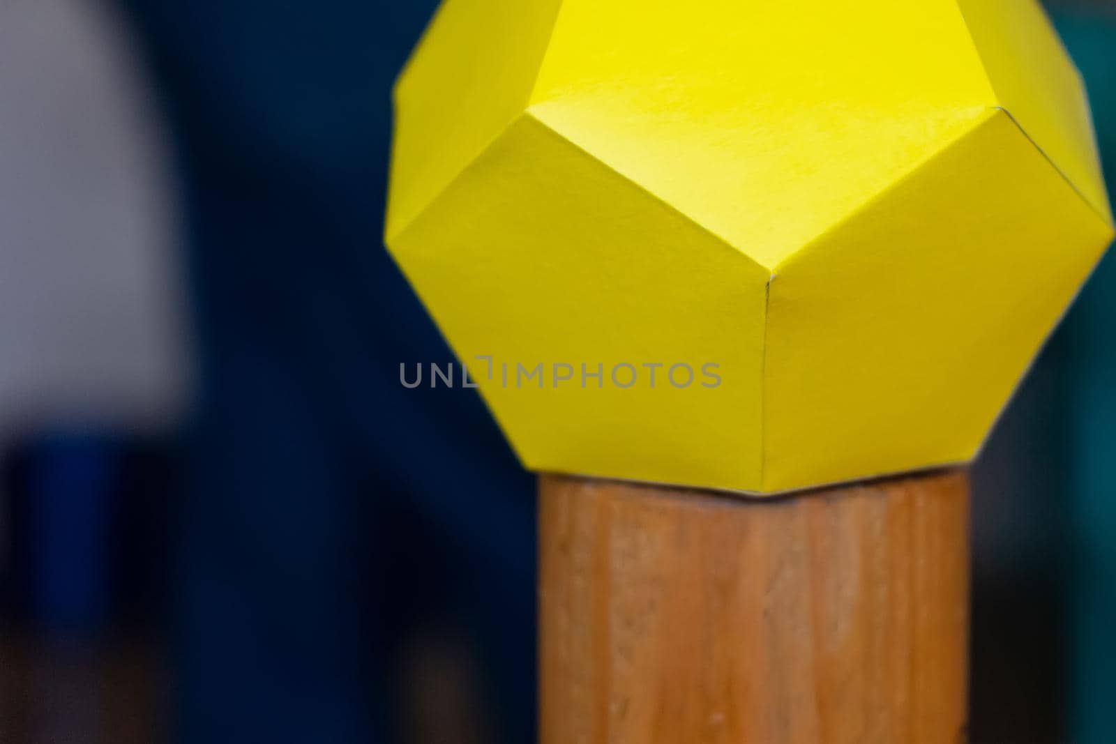 The multifaceted yellow figure is made of many yellow paper pentagons on a wooden stand. Selective focus