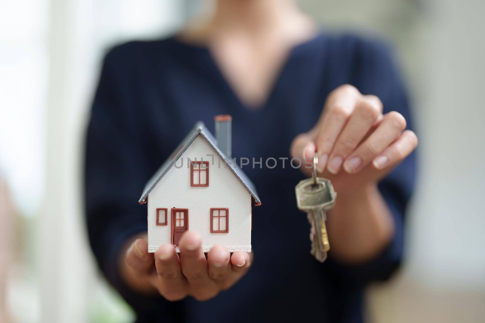 Asian female bank employee handing over a house and keys to a client after signing a contract on paperwork. by Manastrong