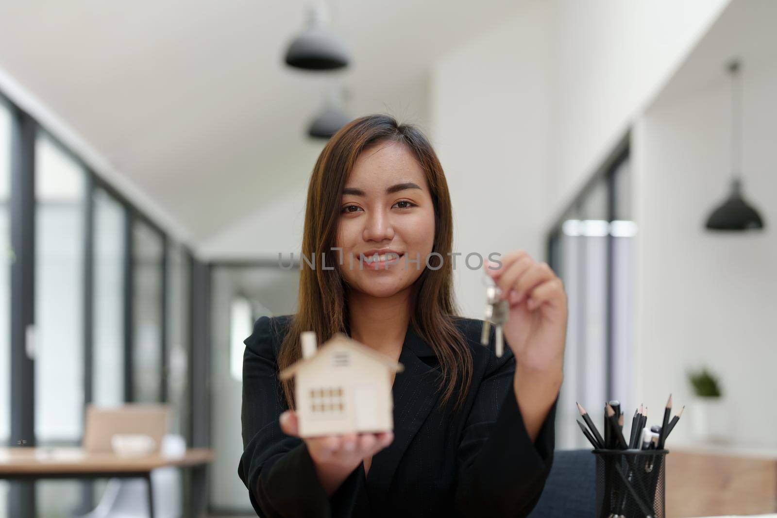 Portrait of an Asian female bank employee handing over a house and keys to a client after signing a contract on paperwork. by Manastrong