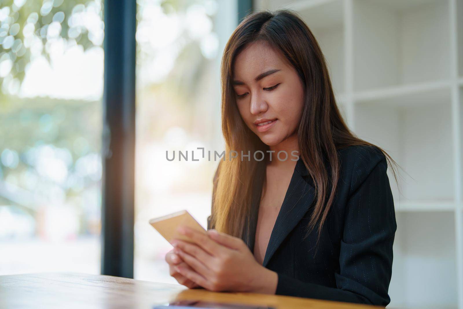 Portrait of an Asian female employee wearing a formal suit using a mobile smartphone to do business with coworkers by Manastrong