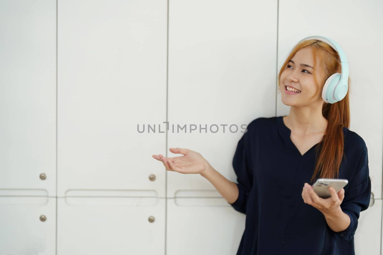 portrait of a young Asian woman with blonde hair wearing over-ear headphones listening to music for relax while taking a break from boring day activities by Manastrong