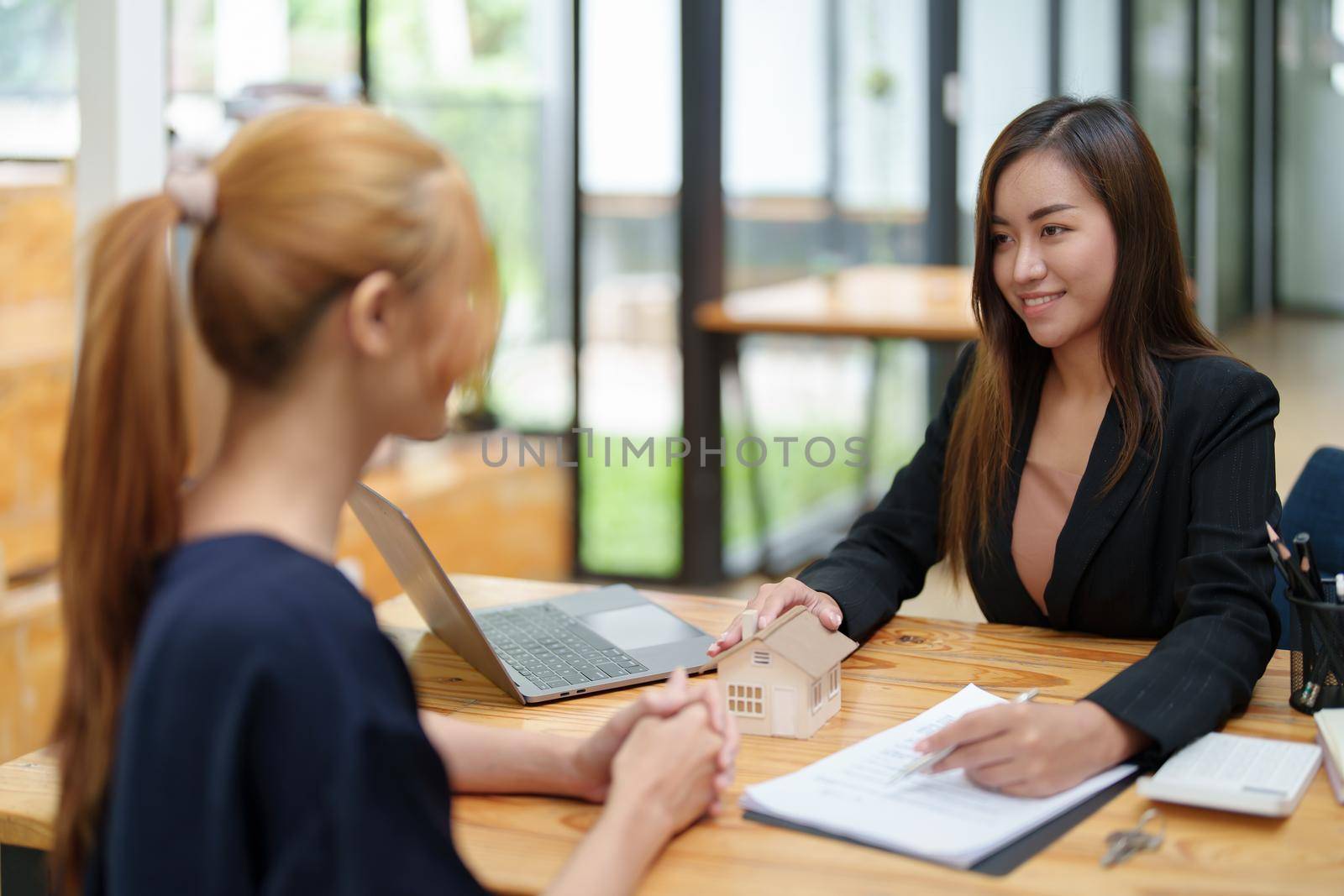 Portrait of an Asian female bank employee asking a customer to read the contract before signing to agree to buy a house, real estate concepts.