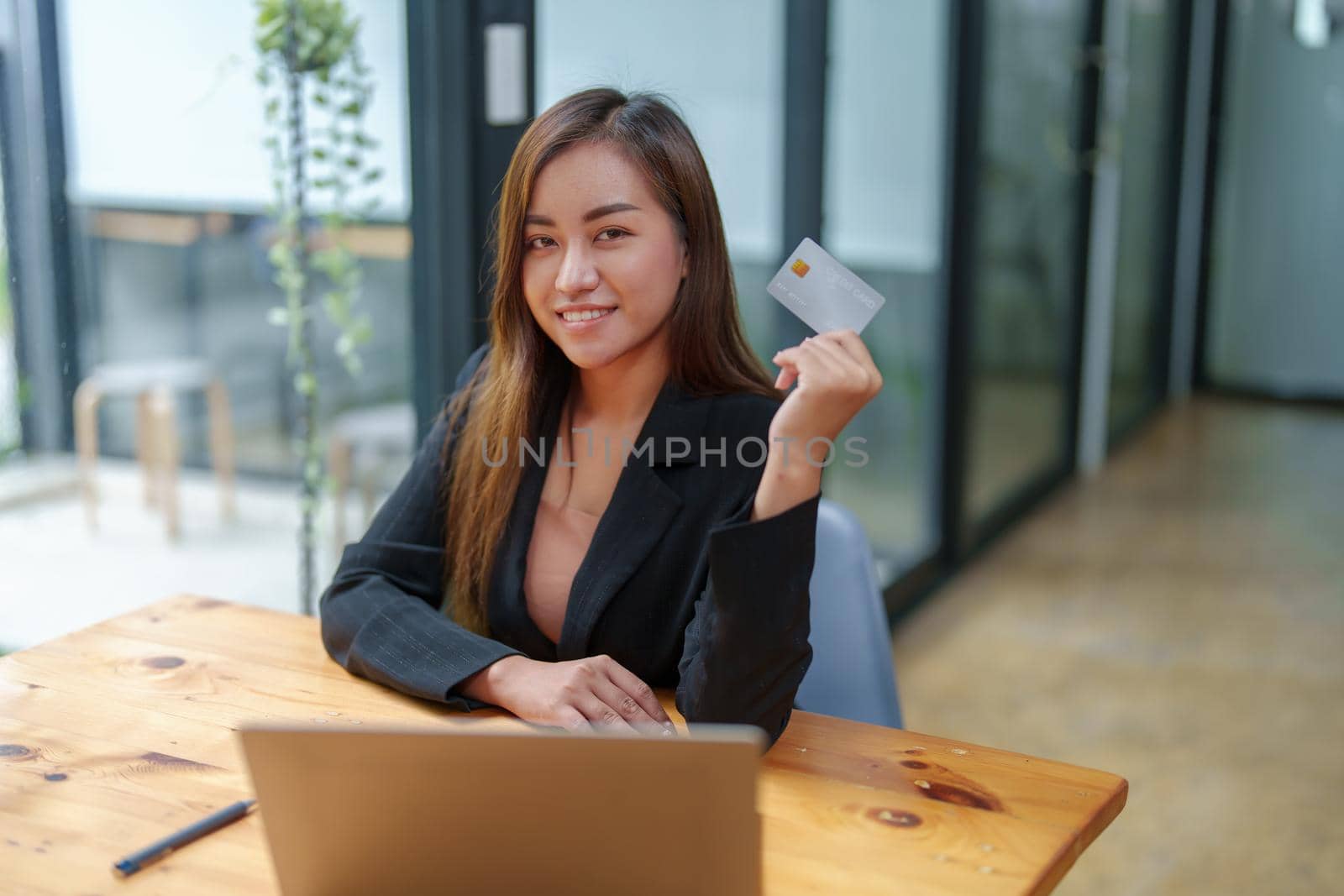 Portrait of a young Asian woman in a suit using credit card and computer laptop for online shopping by Manastrong
