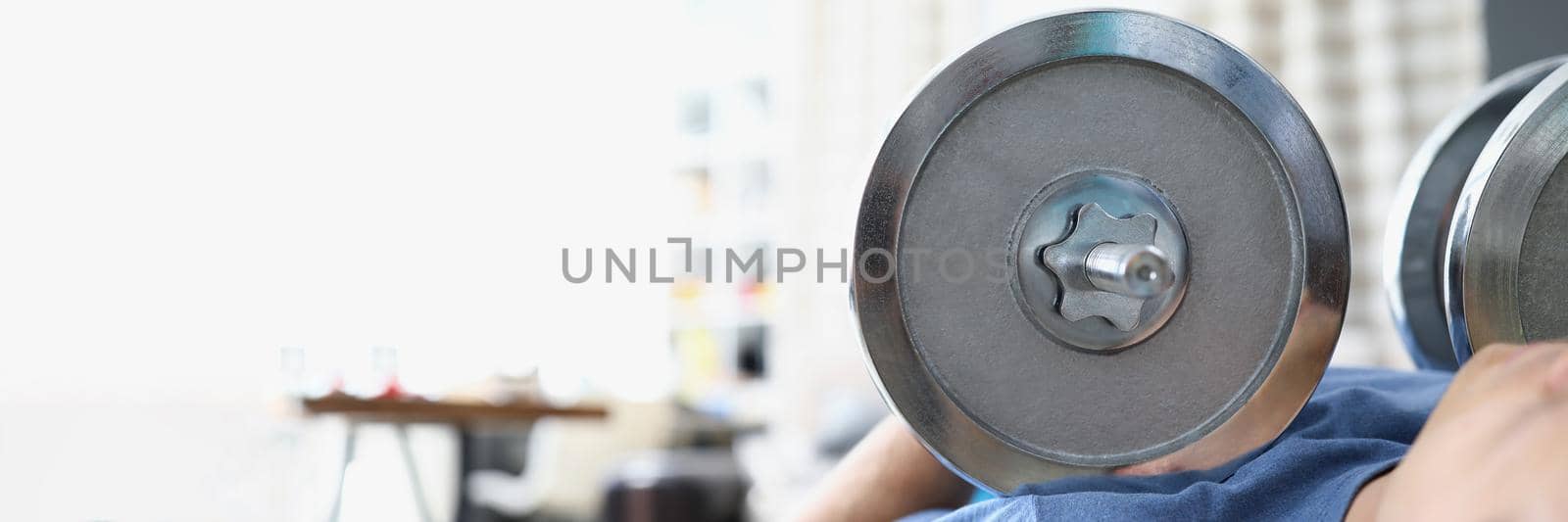 Man lift heavy metal dumbbell laying on training machine by kuprevich