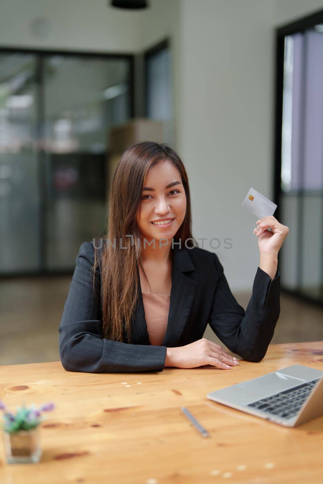 Portrait of a young Asian woman in a suit using credit card and computer laptop for online shopping.