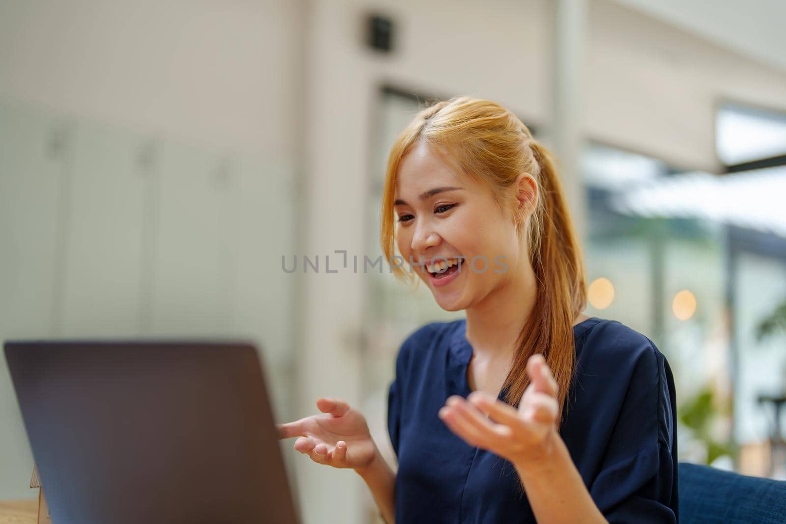 Portrait of an Asian woman using a computer for video conferencing with colleagues to pitch ideas and projects. while working at home by Manastrong