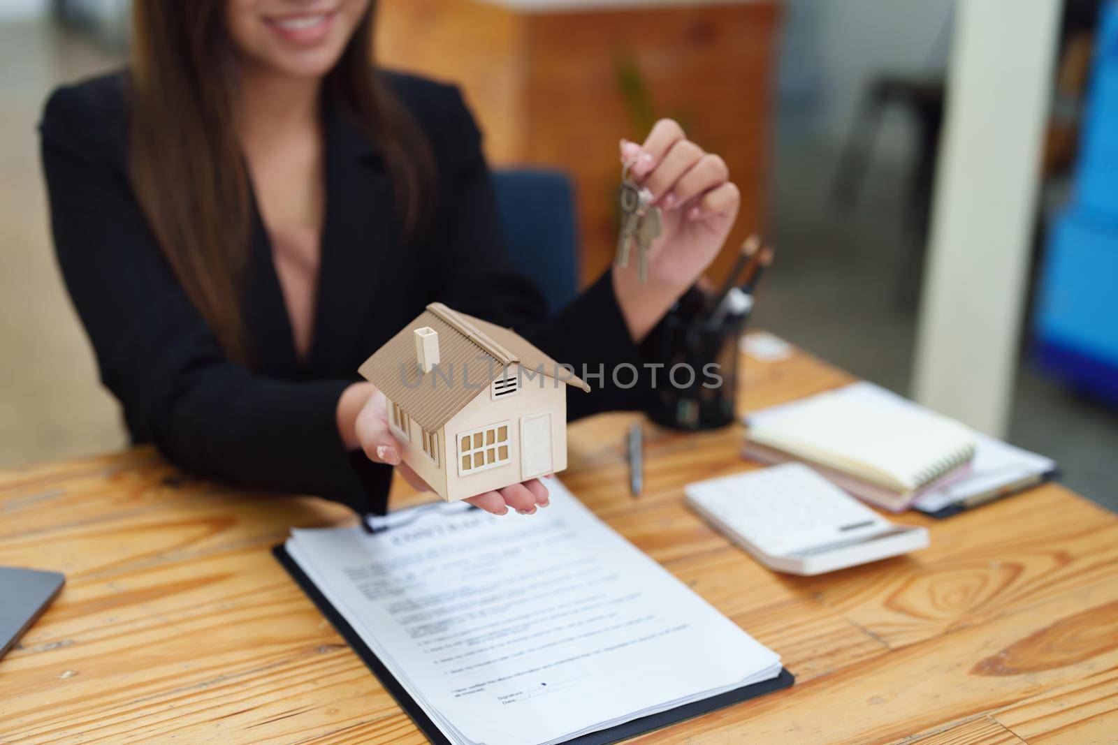 Asian female bank employee handing over a house and keys to a client after signing a contract on paperwork. by Manastrong