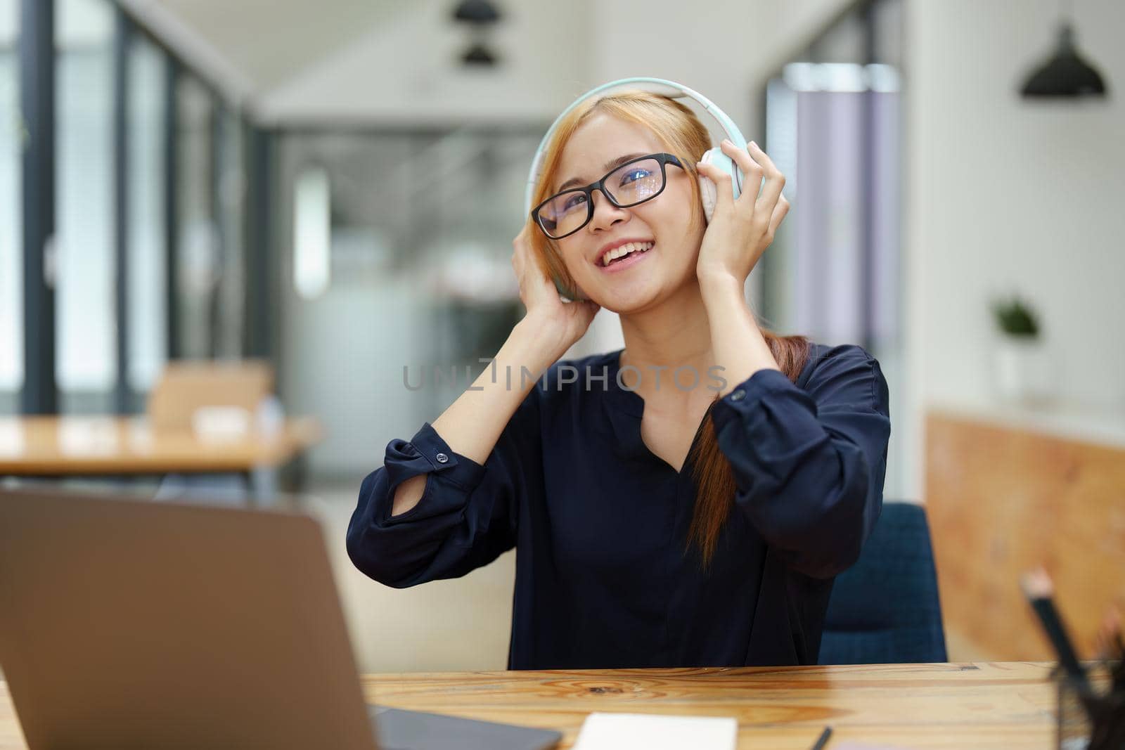 portrait of a young Asian woman with blonde hair wearing over-ear headphones listening to music to relax while taking a break from boring day activities by Manastrong