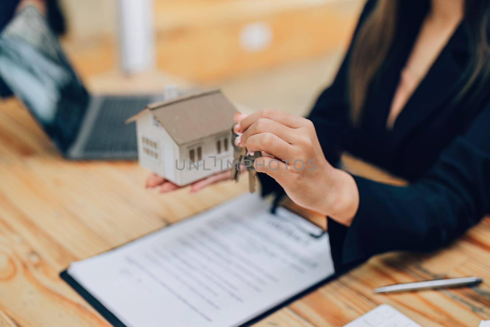 Asian female bank employee handing over a house and keys to a client after signing a contract on paperwork. by Manastrong