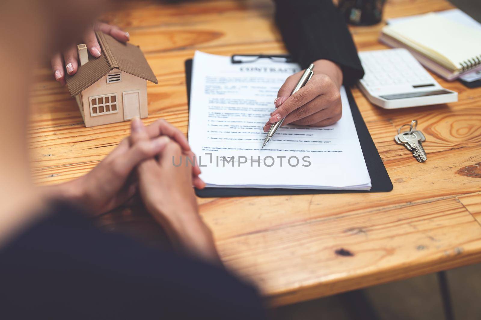 Asian female bank employee asking a customer to read the contract before signing to agree to buy a house, real estate concepts.