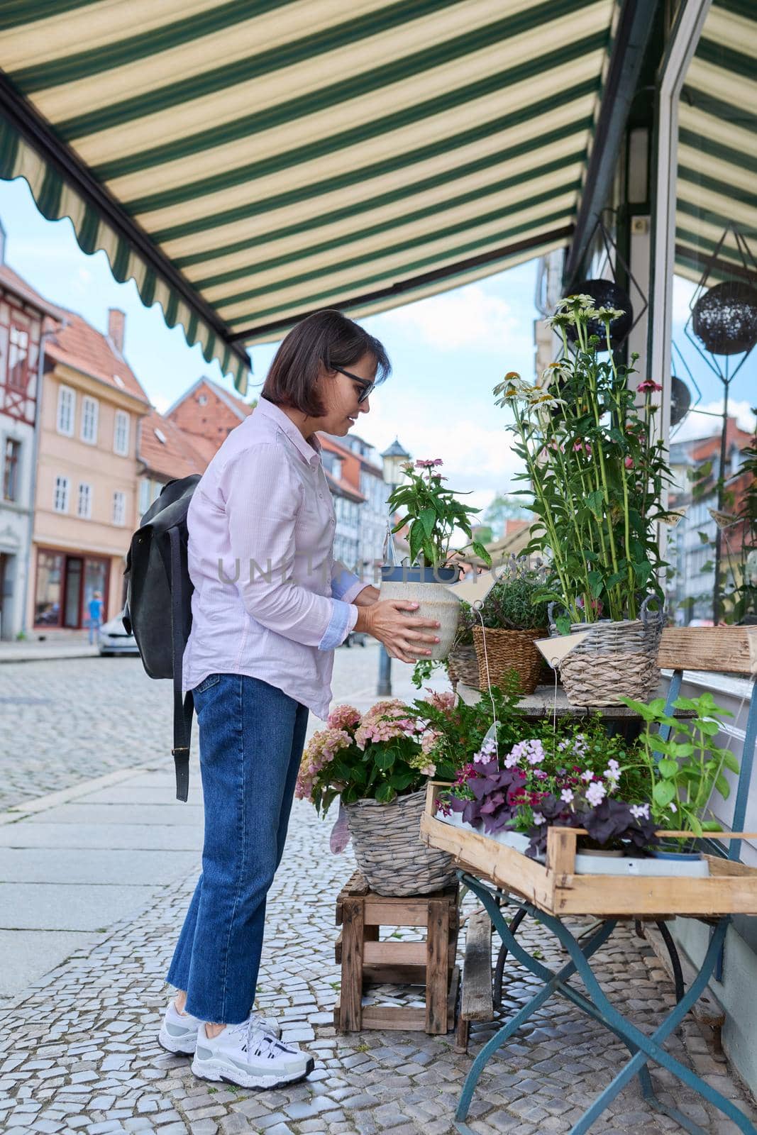 Woman shopping choosing pot with plant in store, on an outdoor rack by VH-studio