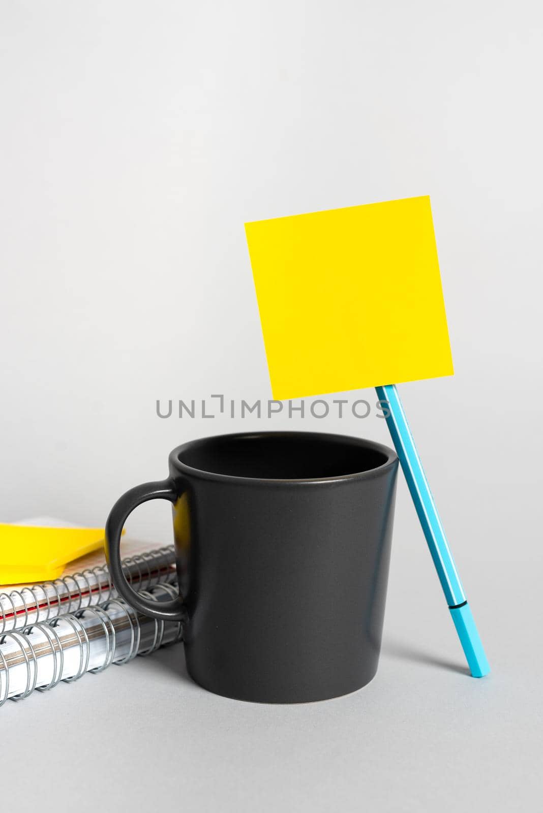 Cup, Pen, Notebooks And Sticky Note With Important Message On Desk. Mug, Pencil And Crutial Announcement On Table. Coffee, Ball Point And Critical Information On Paper. by nialowwa