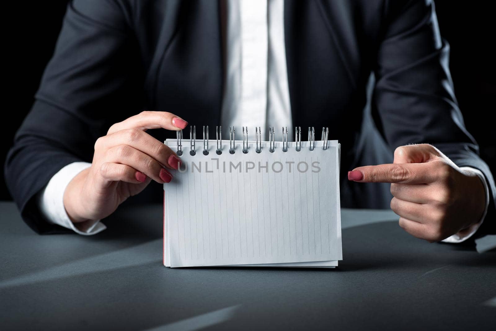 Businesswoman Holding Note With Important Message And Pointing With One Finger. Woman Having Notebook With Crutial Information. Executive Showing Critical Data On Paper. by nialowwa