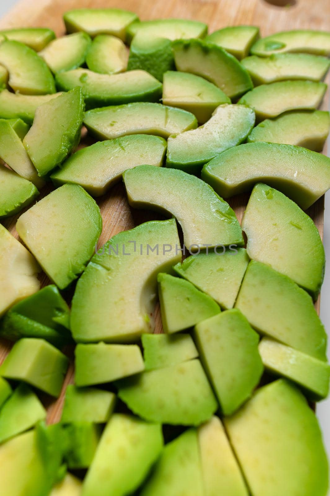 sliced avocado into small pieces lie on a cutting wooden board. food background.