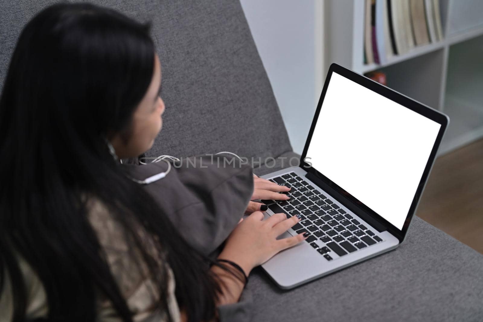 Asian girl lying on comfortable sofa and using laptop computer. by prathanchorruangsak