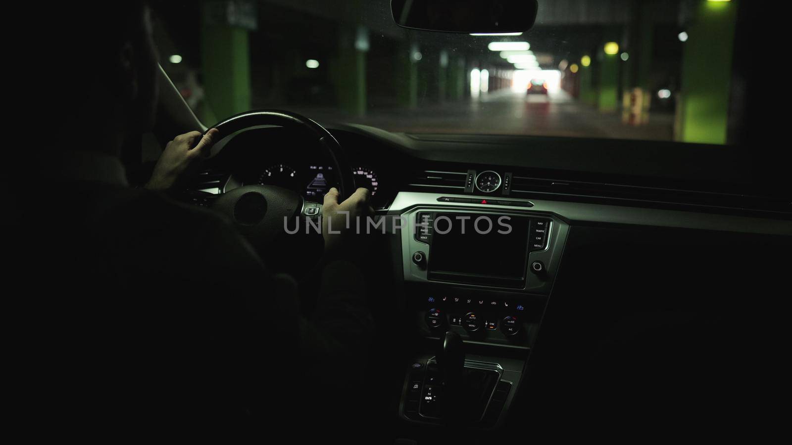 Man driving car on parking space, hands turning steering wheel. Adult man rides in modern car by underground parking. Man driving car through an underground parking lot looking for a place to park.