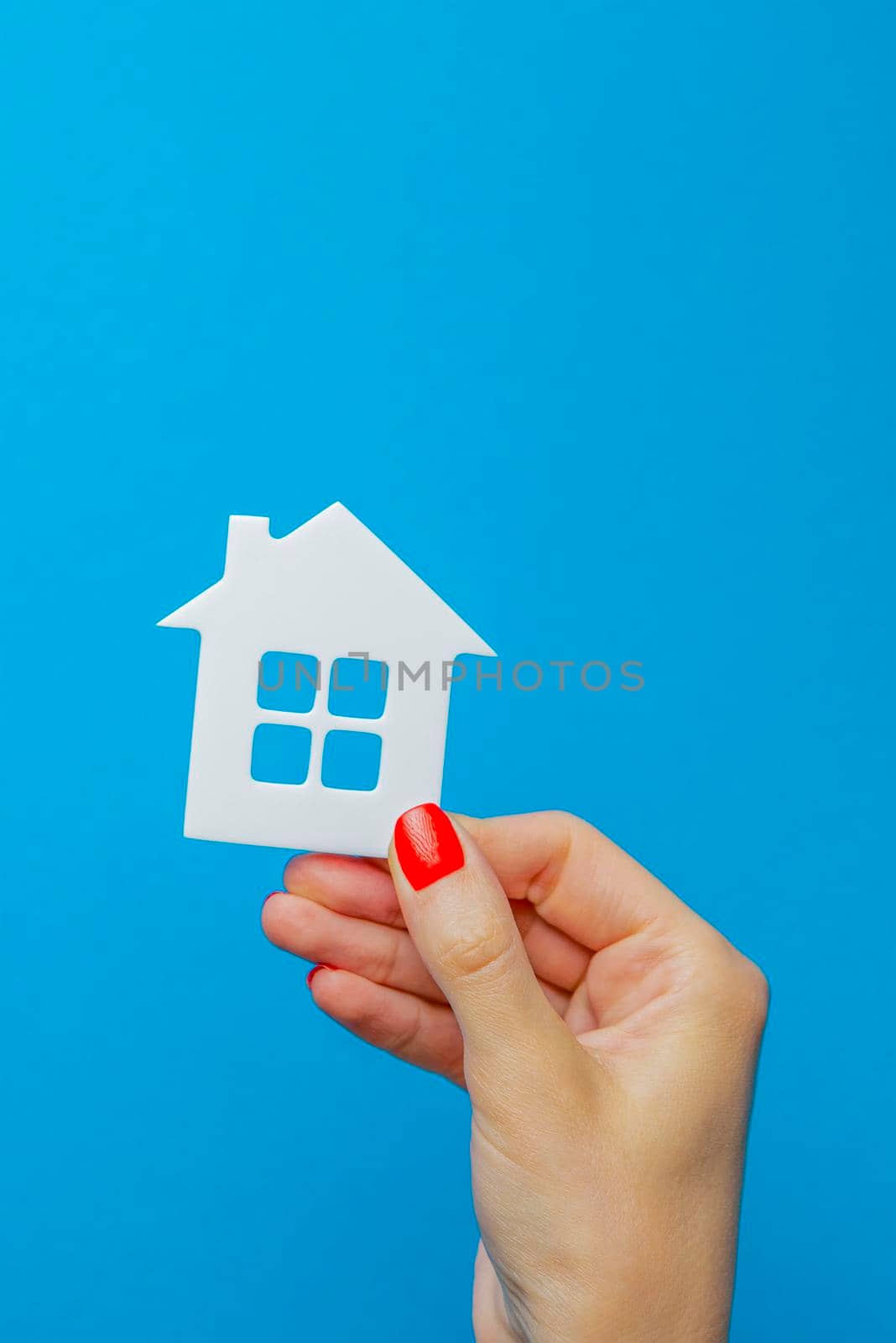 House as a gift. Toy house with a gift bow in hand. Real estate gift concept on blue background. Postcard for printing, banner with place for text.
