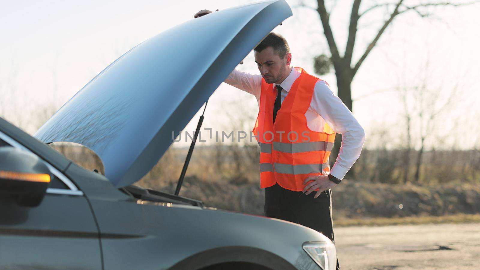 Disappointed man in formal outfit opening bonnet of broke down car to check engine. Sad businessman standing near car opened the hood. Car accident on the road. Emergency stop sign. by uflypro