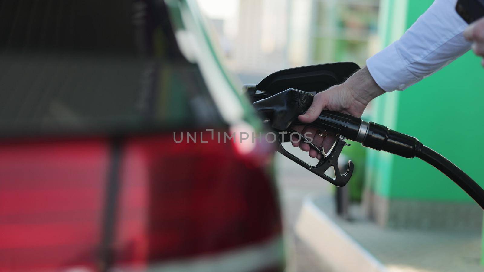 Unrecognizable businessman refueling car from gas station. Senior is refueling car at sunset. Caucasian businessman filling benzine gasoline fuel in car at gas station. Petrol prices concept.