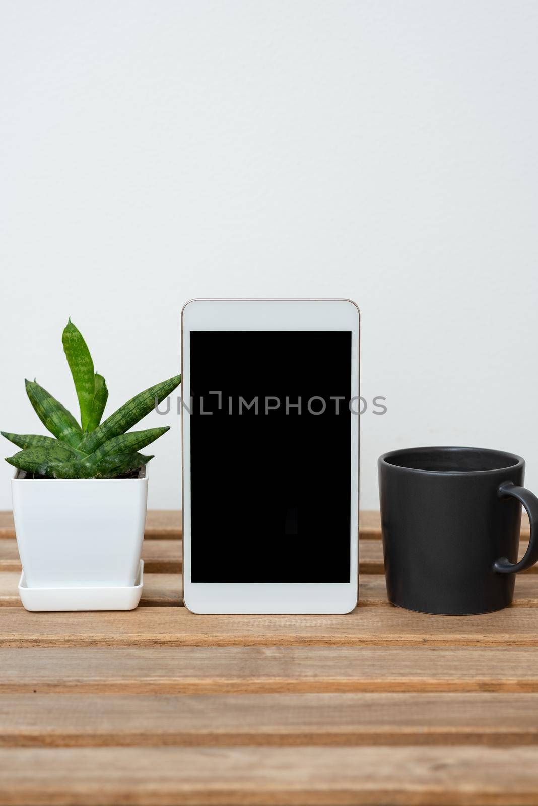 Tablet With Important Informations On Table With Plant And Cup Of Coffee. Crutial Announcements Presented On Cellphone Screen On Desk With Flower And Mug. by nialowwa