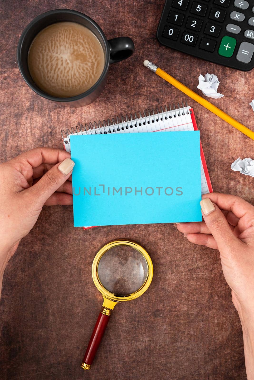 Hands Of Woman Having Pastel Color Sheet With Copy Space, Coffee Cup And Stationery Over Wooden Background. Businesswoman Displaying Business Branding And Promotion Ideas. by nialowwa