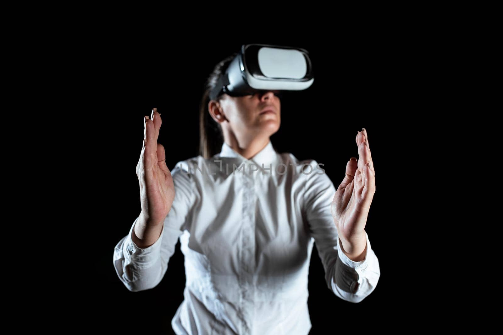 Businesswoman Wearing Virtual Reality Goggles And Enjoying Simulator. Elegant Woman Using Futuristic Gadget Gesturing And Presenting Modern Innovative Technology. by nialowwa