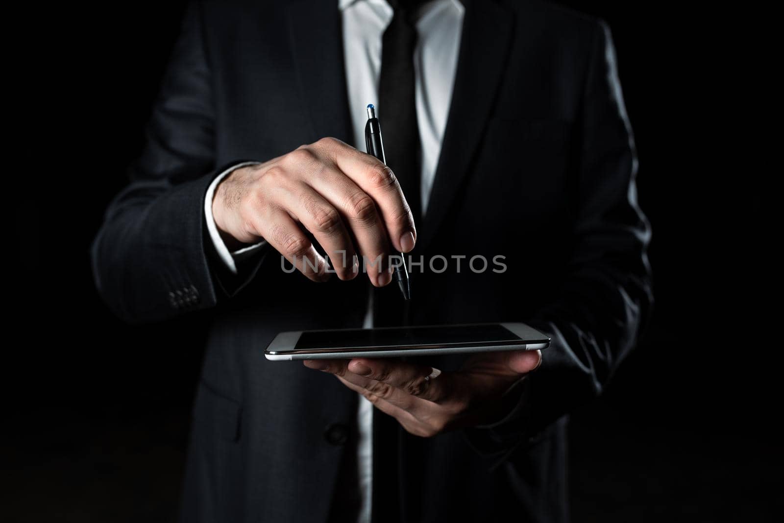 Businessman Holding Tablet In One Hand With Other Pointing Important Message With Pen. Executive In Suit Having Cellphone In One Palm And Displaying Crutial Announcement On It by nialowwa