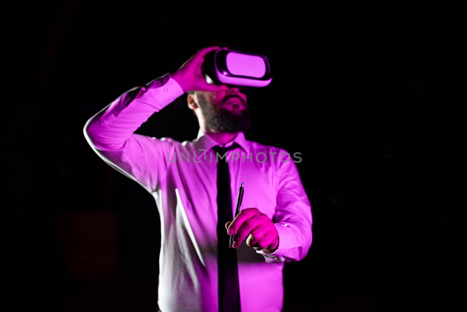 Businessman Wearing Headset Holding Pen While Taking Professional Training Through Wearing Virtual Reality Simulator. Light Falling On Man Presenting Futuristic Technology. by nialowwa