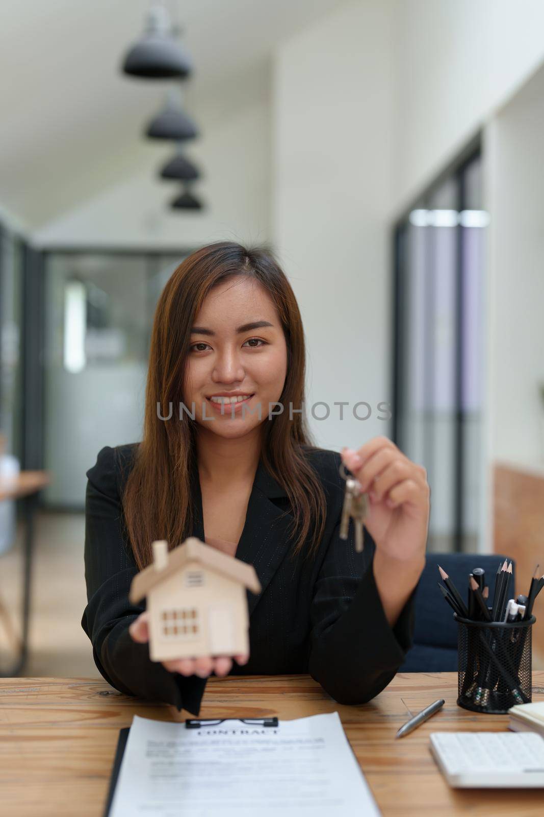 Portrait of an Asian female bank employee handing over a house and keys to a client after signing a contract on paperwork