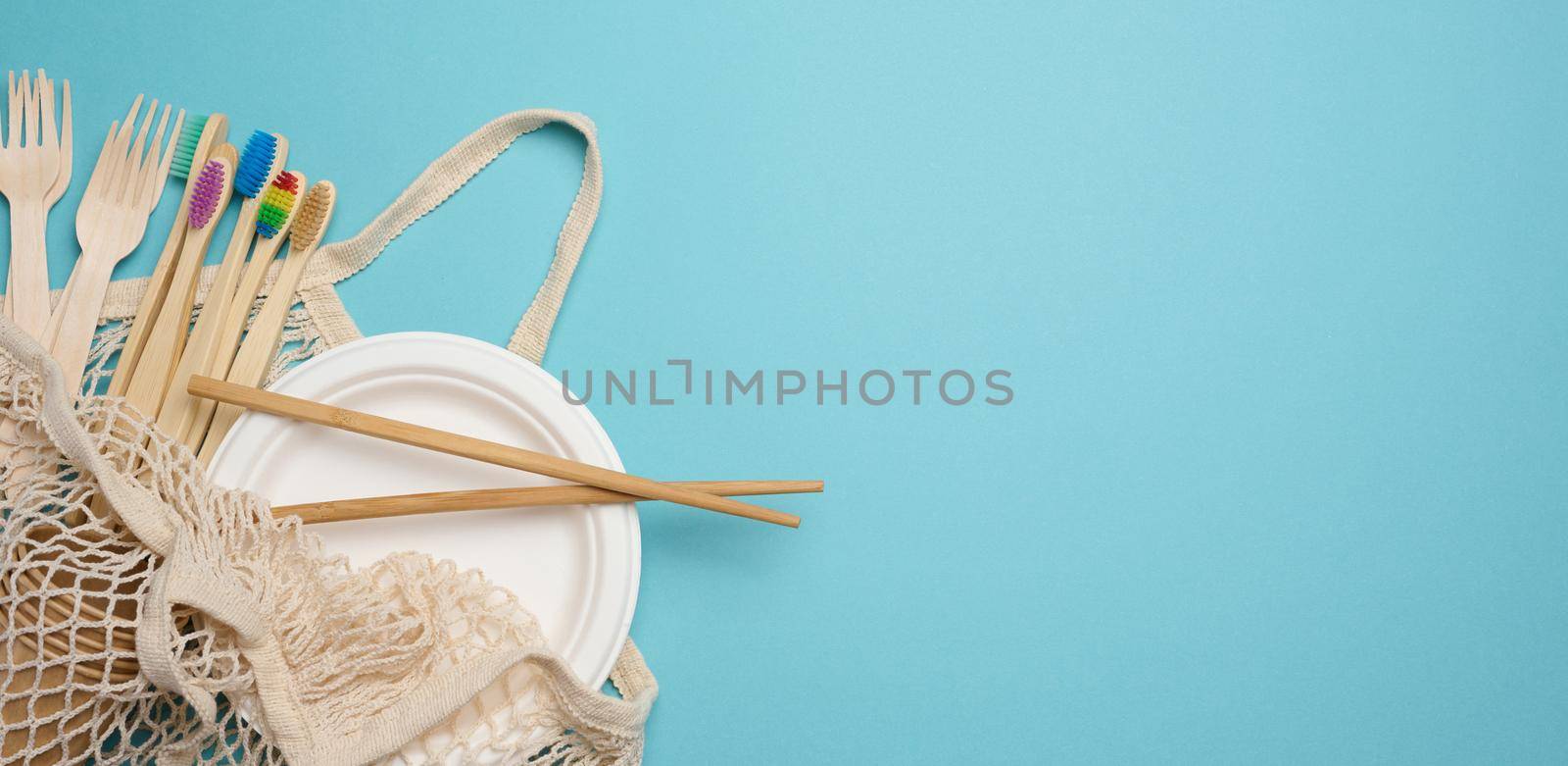 White textile bag and disposable tableware on a blue background. View from above, plastic rejection concept, zero waste. Copy space