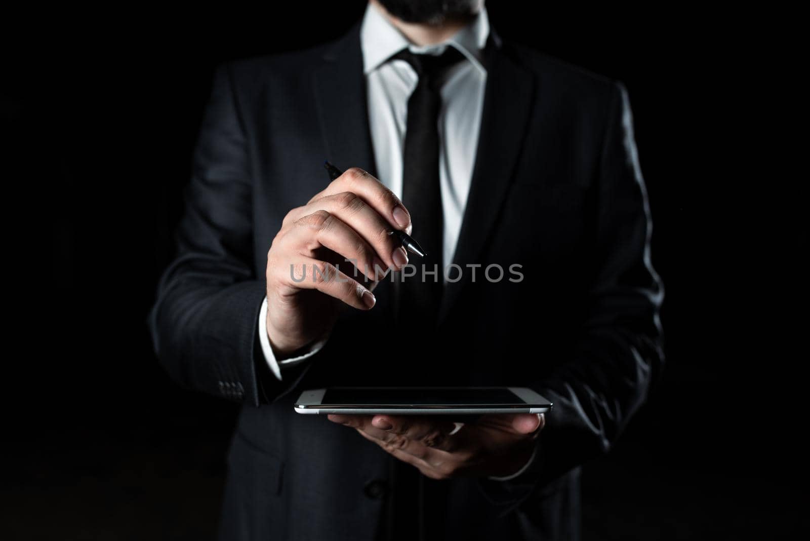 Businessman Holding Tablet In One Hand With Other Pointing Important Message With Pen. Executive In Suit Having Cellphone In One Palm And Crutial Announcement In Another. by nialowwa