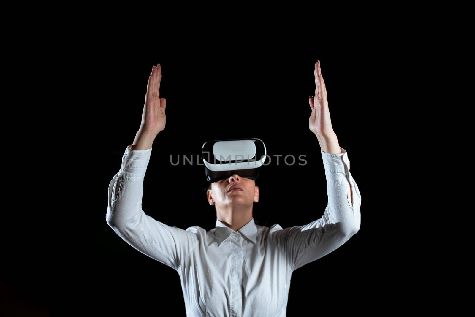 Businesswoman Wearing Virtual Reality Headset And Gesturing While Taking Professional Training. Woman Wearing Futuristic Simulator And Presenting Modern Technology. by nialowwa