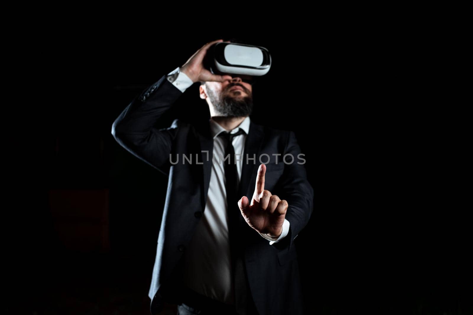 Businessman Wearing Virtual Reality Headset Gesturing And Taking Professional Training Through Simulator. Man In Suit Presenting Modern Technology Of Innovative Learning. by nialowwa