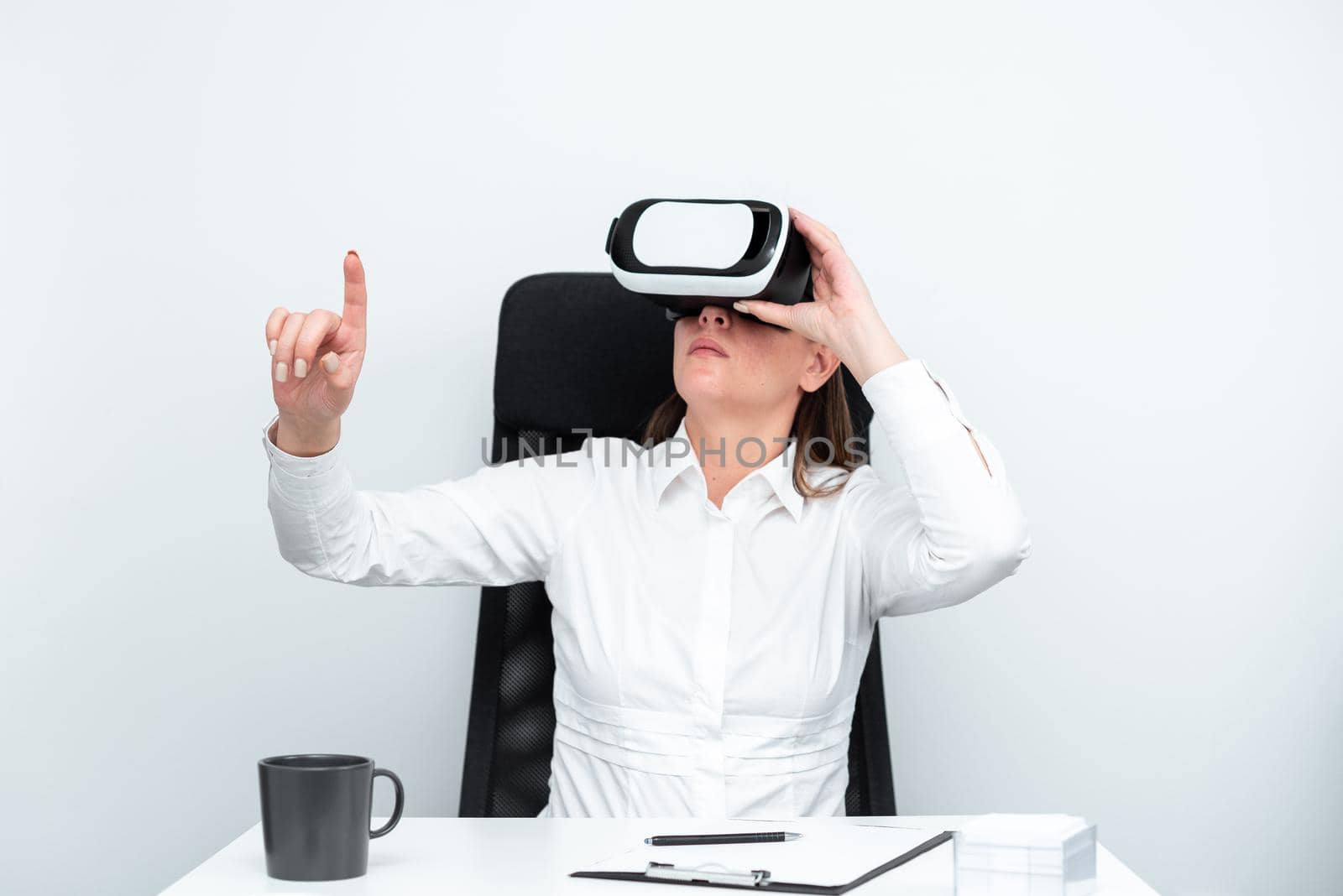 Businesswoman Wearing Virtual Reality Goggles And Learning Professional Skill Through Futuristic Simulation. Woman Gesturing While Sitting At Desk During Modern Training. by nialowwa