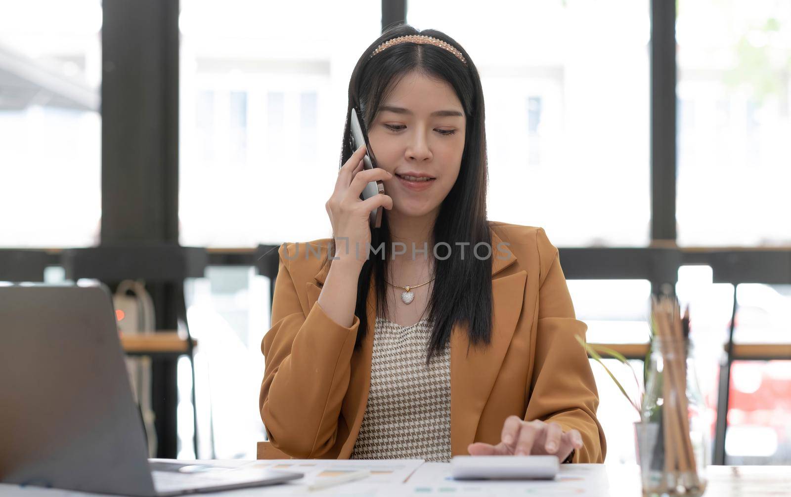 Asian business woman have the joy of talking the phone, and use calculator on the office desk. by wichayada