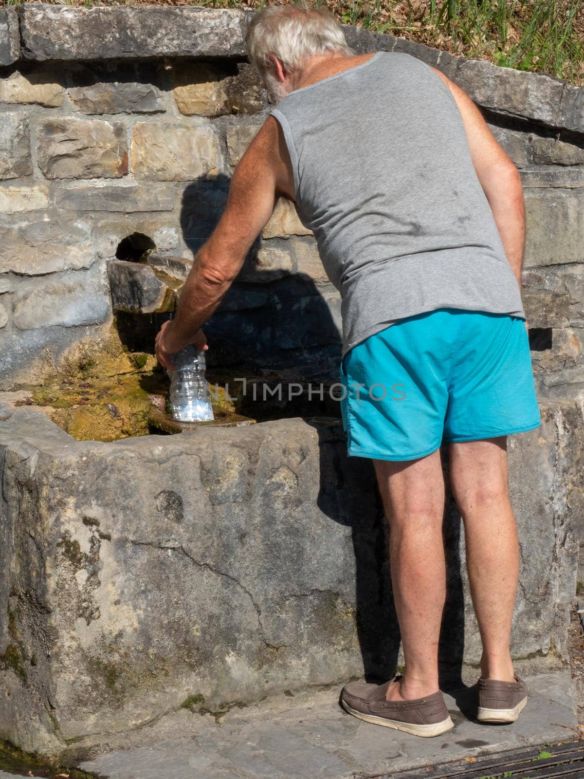 senior caucasian man bottling fresh spring water in a public source by verbano
