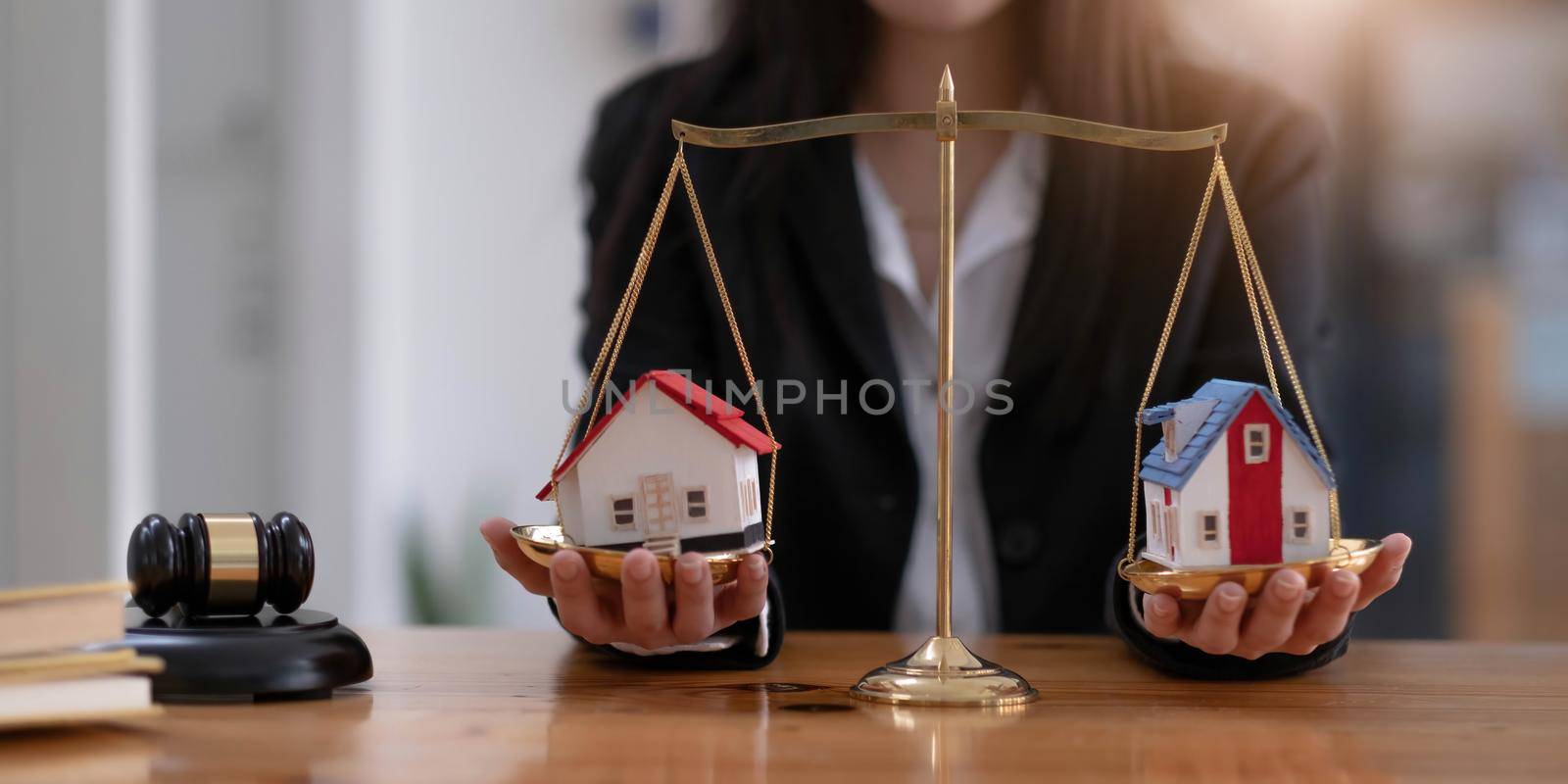 Female lawyer protecting a house model on a scales of justice. Property and legal concept. Houses Litigation. cropped image.