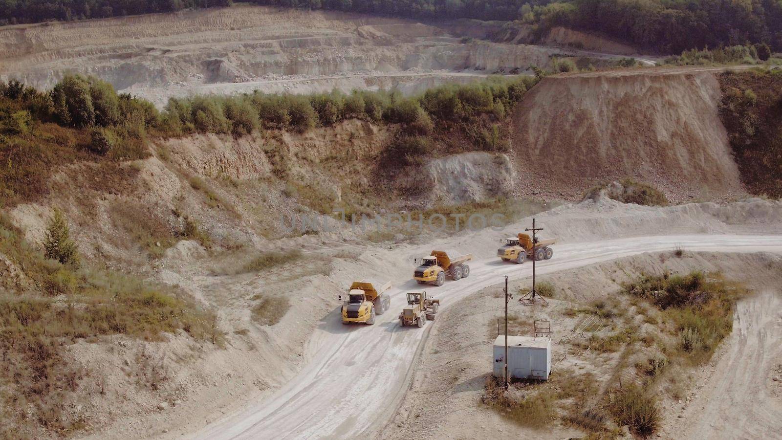 Heavy Dump Trucks At The Coal Mining Area. Aerial view of the quarry mining trucks, heavy industry and machinery concept. Process of transportation of minerals, mining truck is driving along a road by uflypro