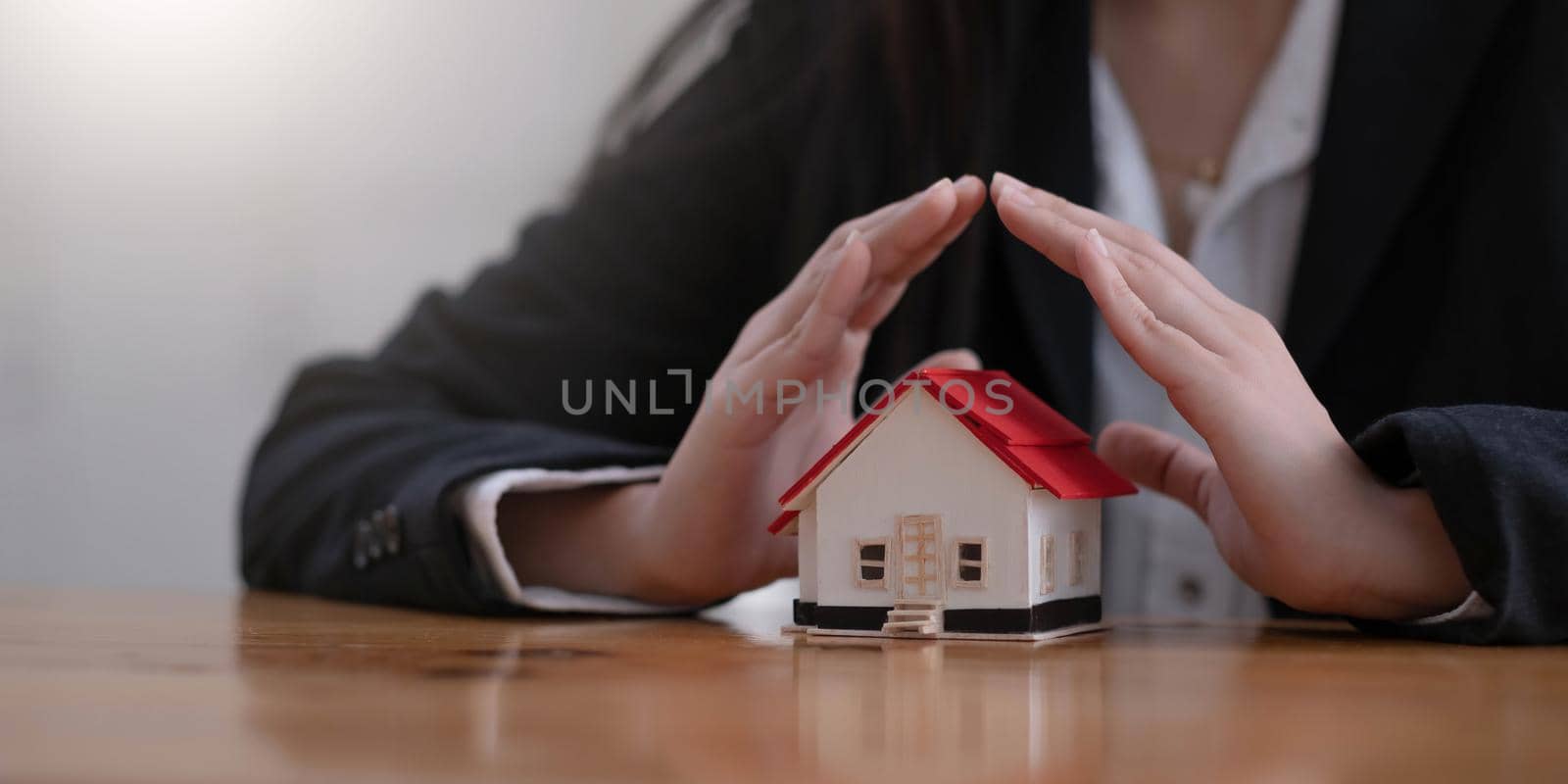 Protect your house concept. Small toy house covered by hands.