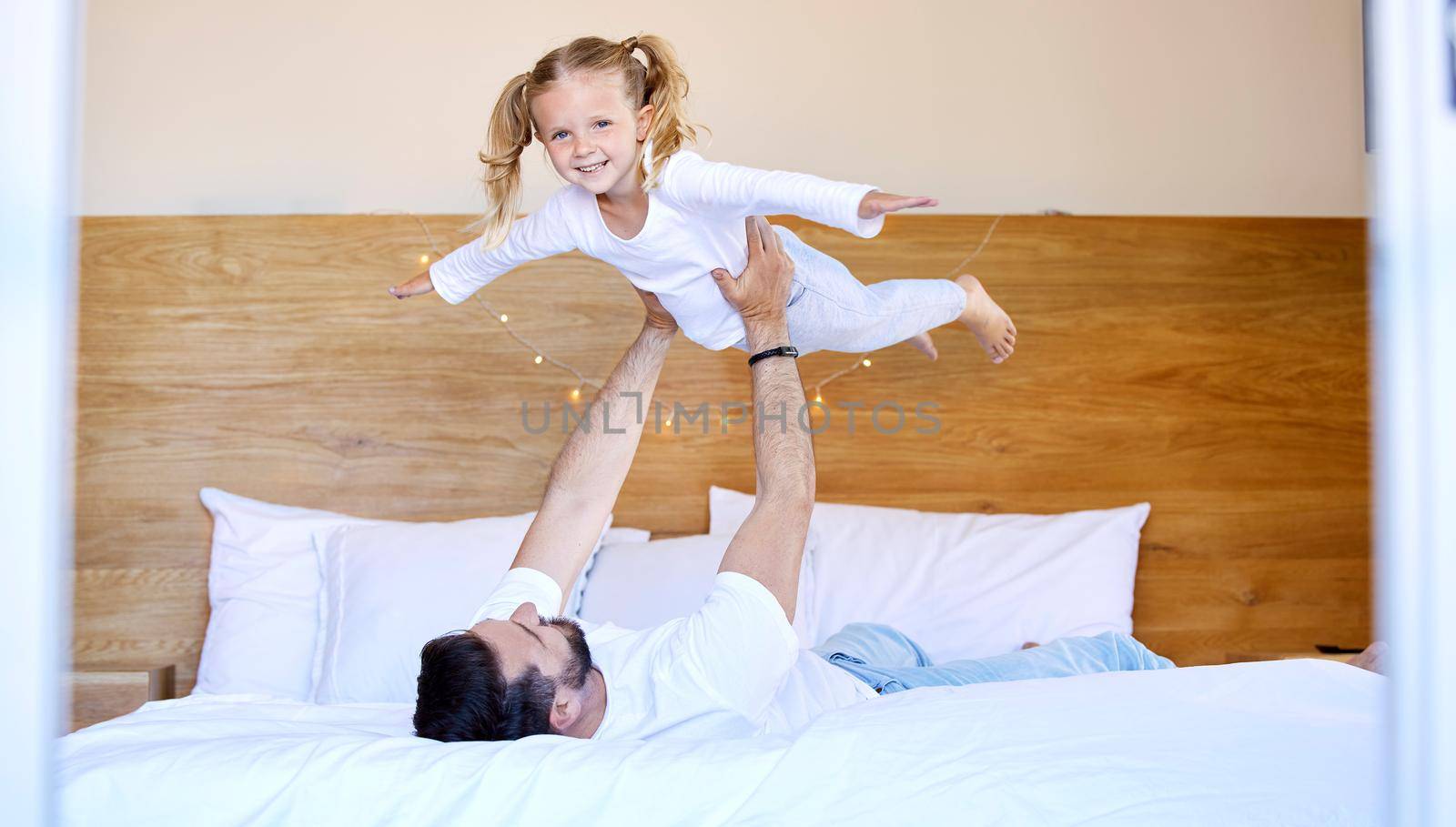 Adorable little girl bonding with her single father at home and pretending she can fly. Caucasian single parent holding and lifting his daughter in the air. Smiling child playing in the bedroom by YuriArcurs