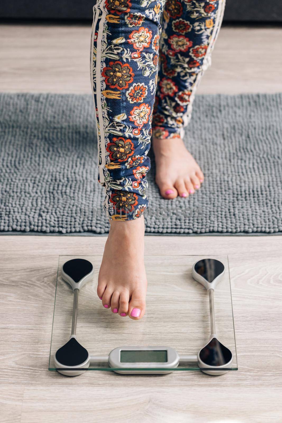 Female feet step on floor scales close up. Woman measuring her body weight by standing on electronic bathroom scale indoors. Girl checks his weight after training at home by uflypro