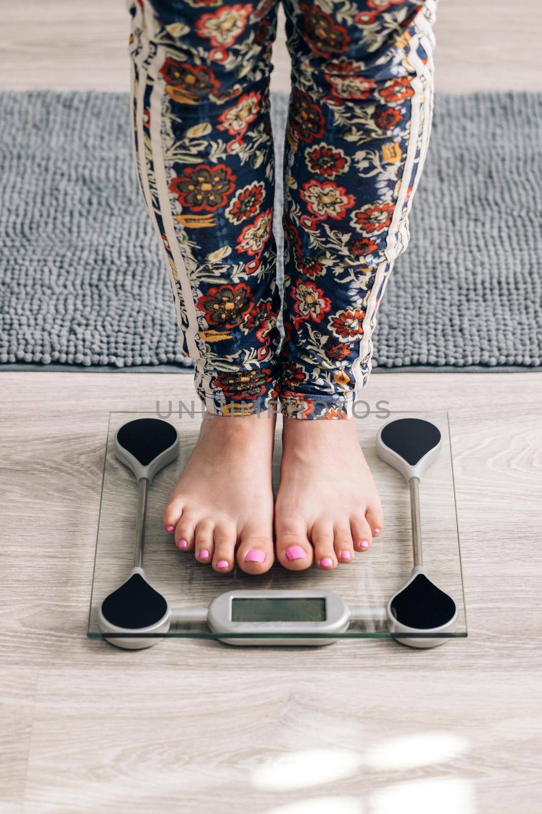 Closeup of barefoot woman using digital scales and checking her weight. Female feet step on floor scales. Concept of dieting, loosing weight and healthy lifestyle.