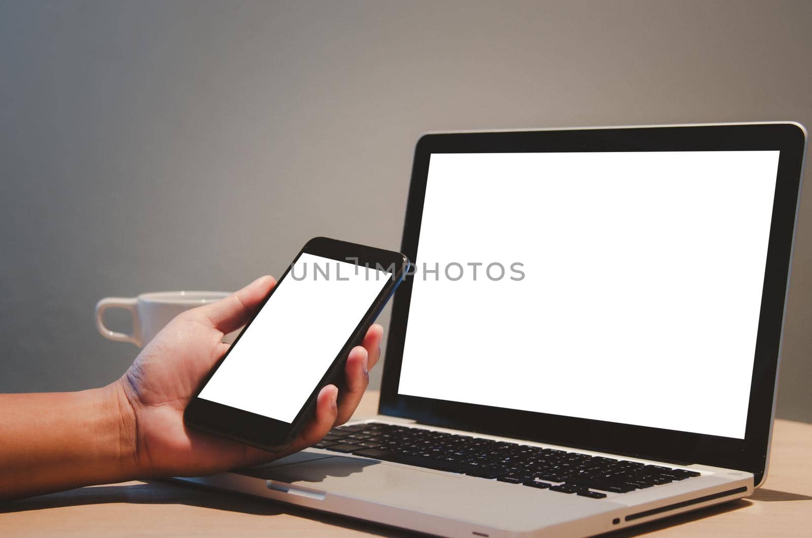 man hand holding mobile smartphone and computer laptop mock up blank screen on desk.
