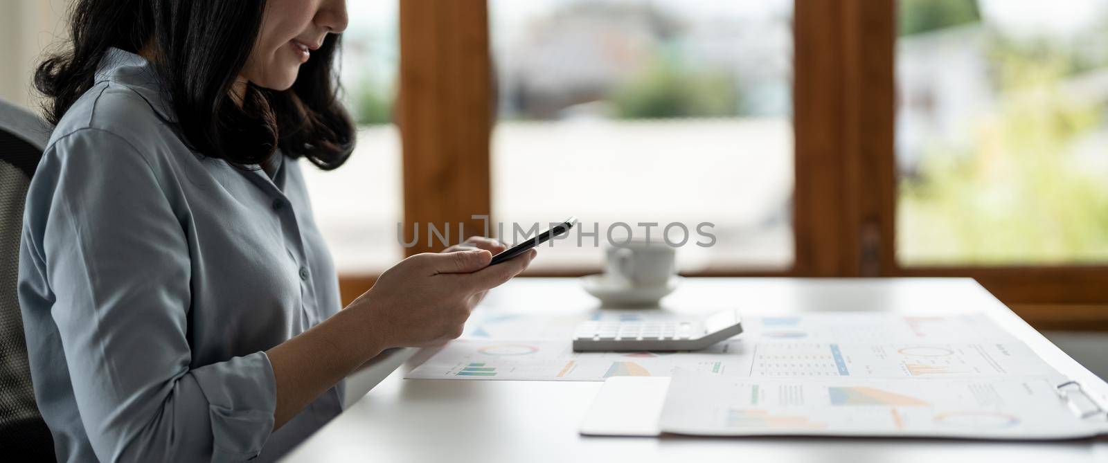 Business asian woman using smartphone for do math finance on wooden desk in office, tax, accounting, financial concept by nateemee