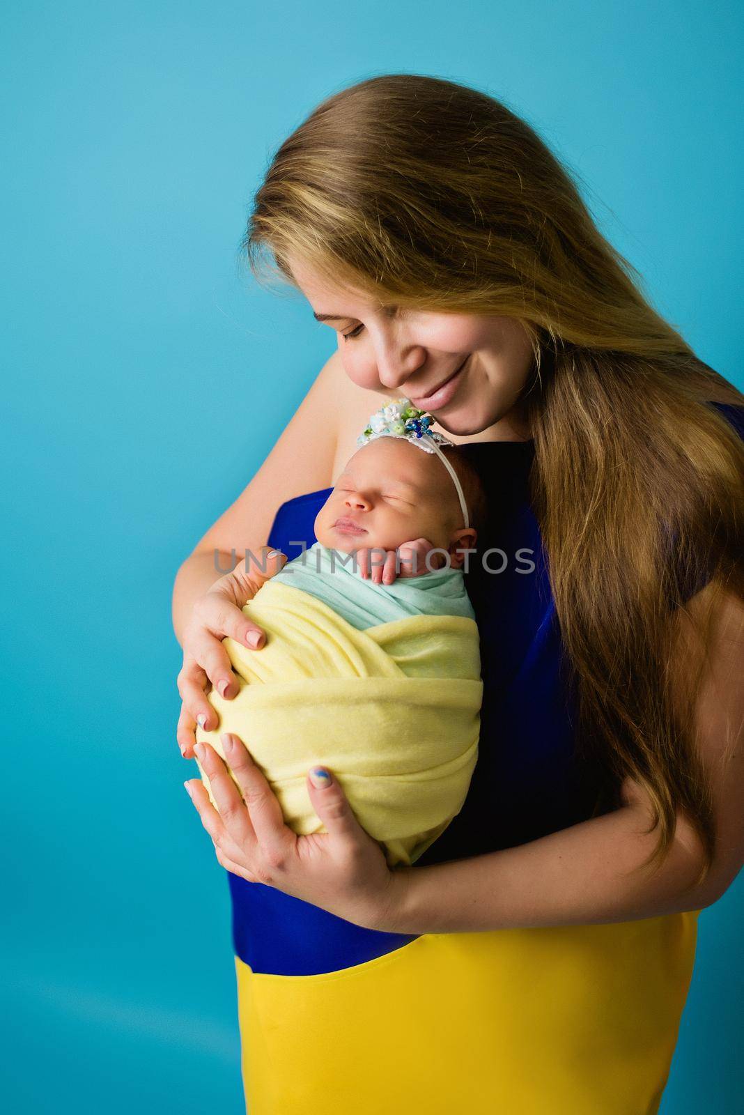 A Ukrainian mother in national yellow blue flag with an infant in the colors during the 2022 war. Close-up in the studio, vertical, insulated background. The most important heroes of women.