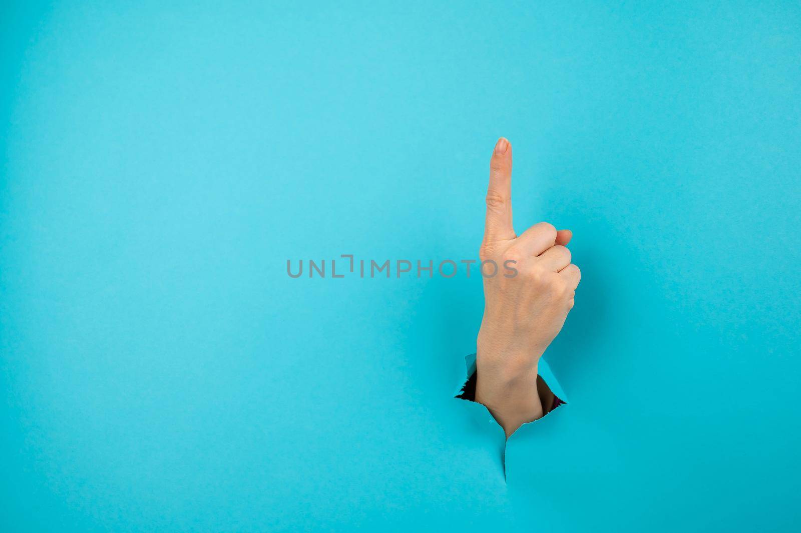 A woman's hand sticking out of a hole from a blue background shows her index finger up